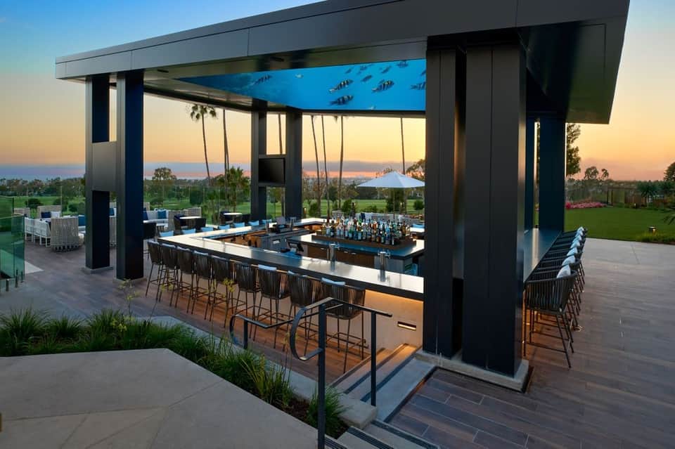 Modern outdoor bar with black columns overlooking landscaped grounds at sunset