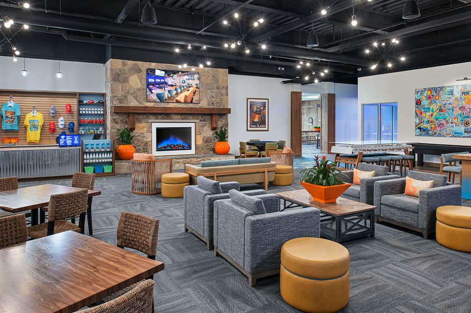 Modern hotel lounge with gray seating, fireplace, stone accent wall, and colorful artwork on exposed beam ceiling