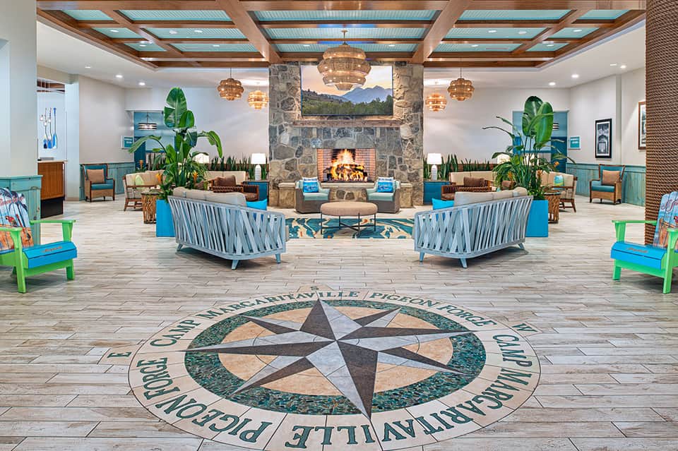 Spacious hotel lobby with compass rose floor design, stone fireplace, hanging chandeliers, and blue seating areas