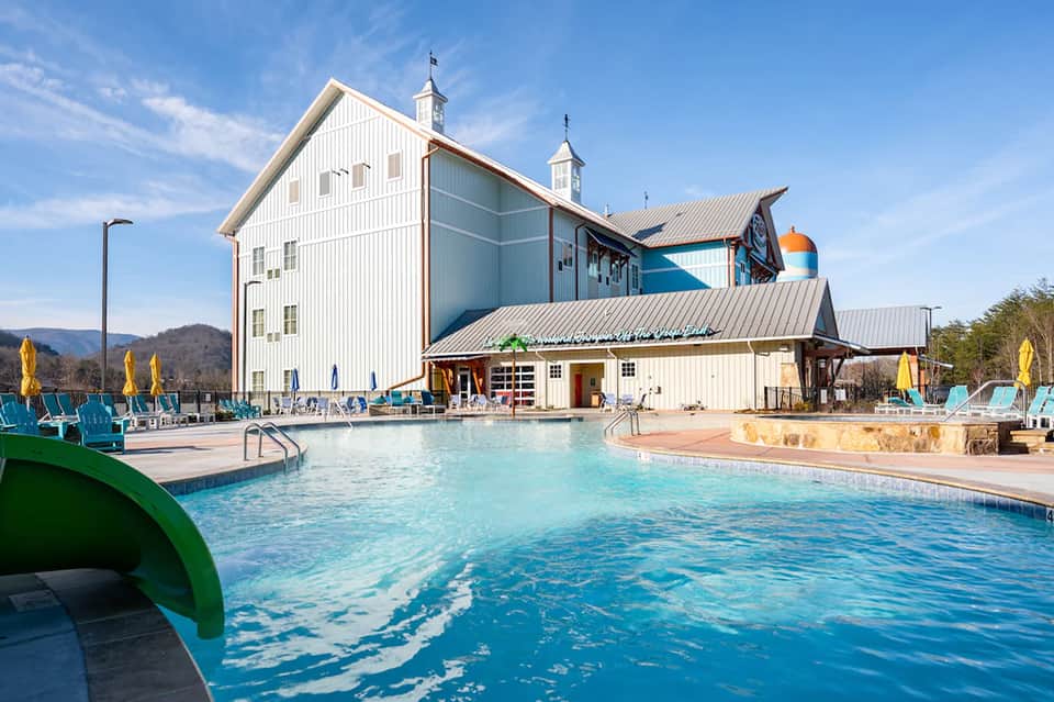 Modern white barn-style resort with outdoor pool, yellow umbrellas, and mountain views
