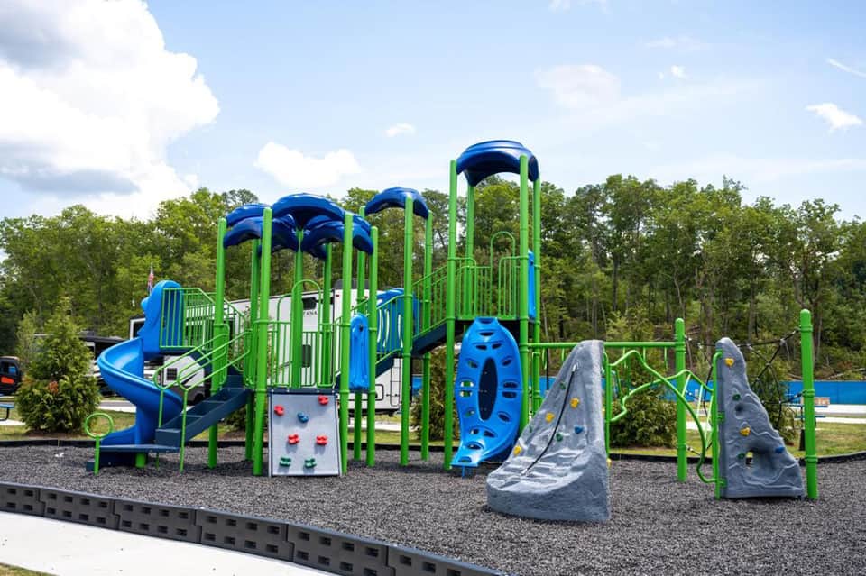 Colorful playground with blue and green climbing structures, slides, and rock walls on rubberized surface