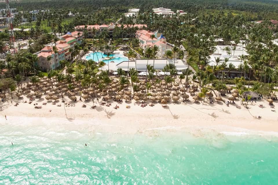 Aerial view of beachfront resort with palm trees, pool, and turquoise ocean waters