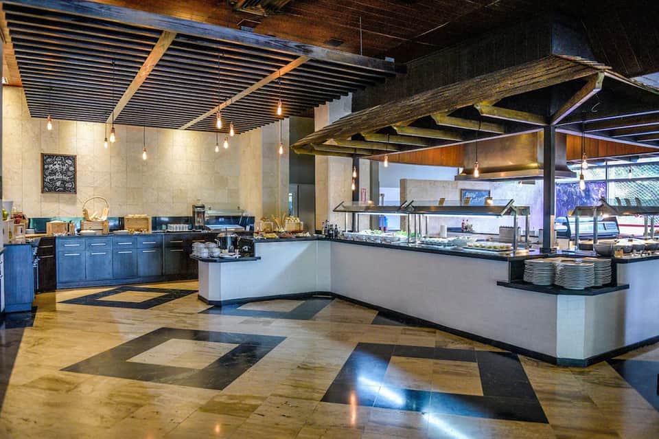 Modern restaurant kitchen with blue cabinetry, white counters, pendant lighting, and geometric floor patterns