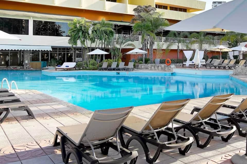 Large resort pool with loungers, umbrellas, and multi-story building backdrop