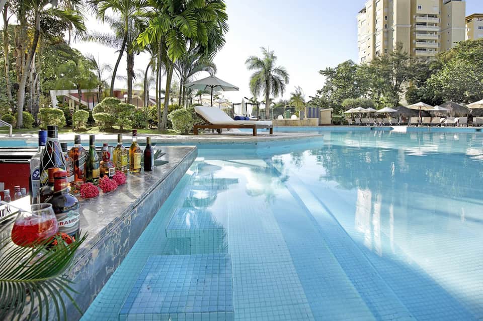 Luxury resort pool with palm trees, loungers, umbrellas, and tropical landscaping under clear sky