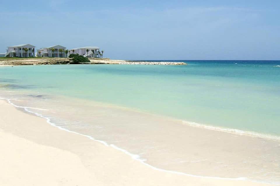 Pristine turquoise beach with white sand and beachfront homes on the horizon