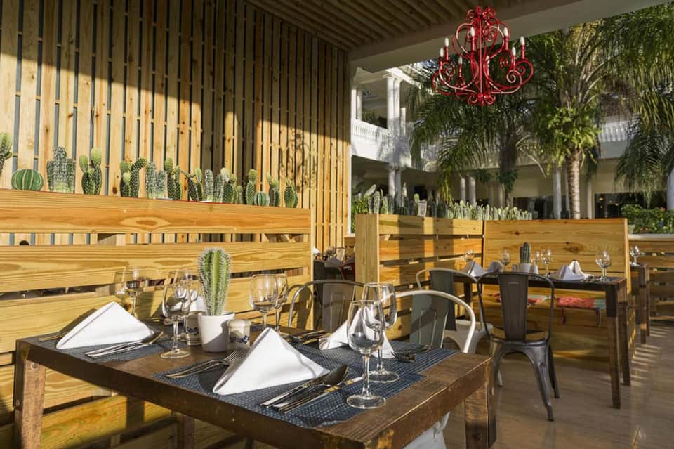 Upscale outdoor dining area with wooden slat walls, potted cacti, and elegant table settings under a red chandelier