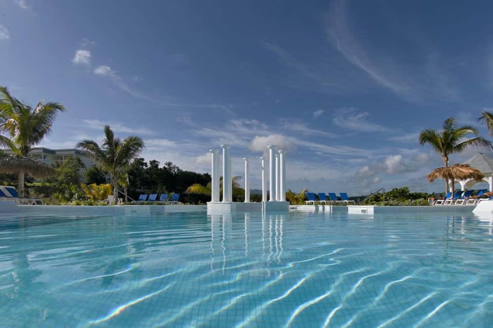 Resort infinity pool with white columns and palm trees under clear blue sky