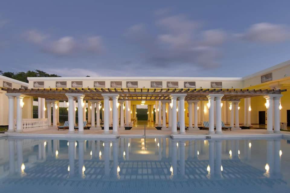Elegant white columned pavilion with yellow beams reflected in illuminated pool at dusk