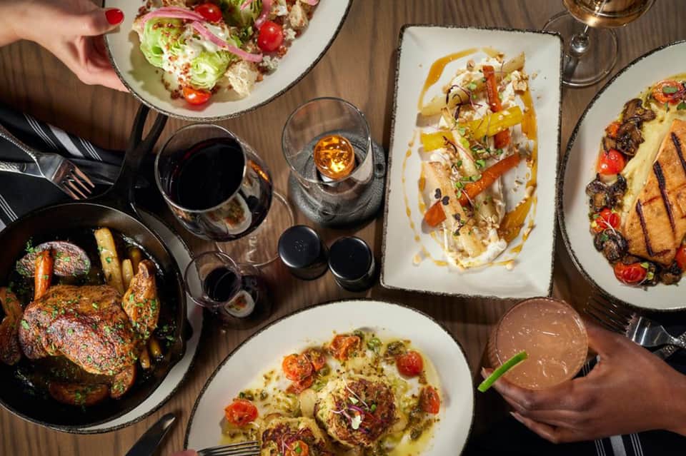 Upscale dining table with gourmet plated dishes, salads, grilled meats, and wine glasses