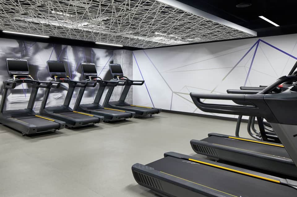 Modern gym with treadmills and exercise equipment, white industrial ceiling, black and yellow accents