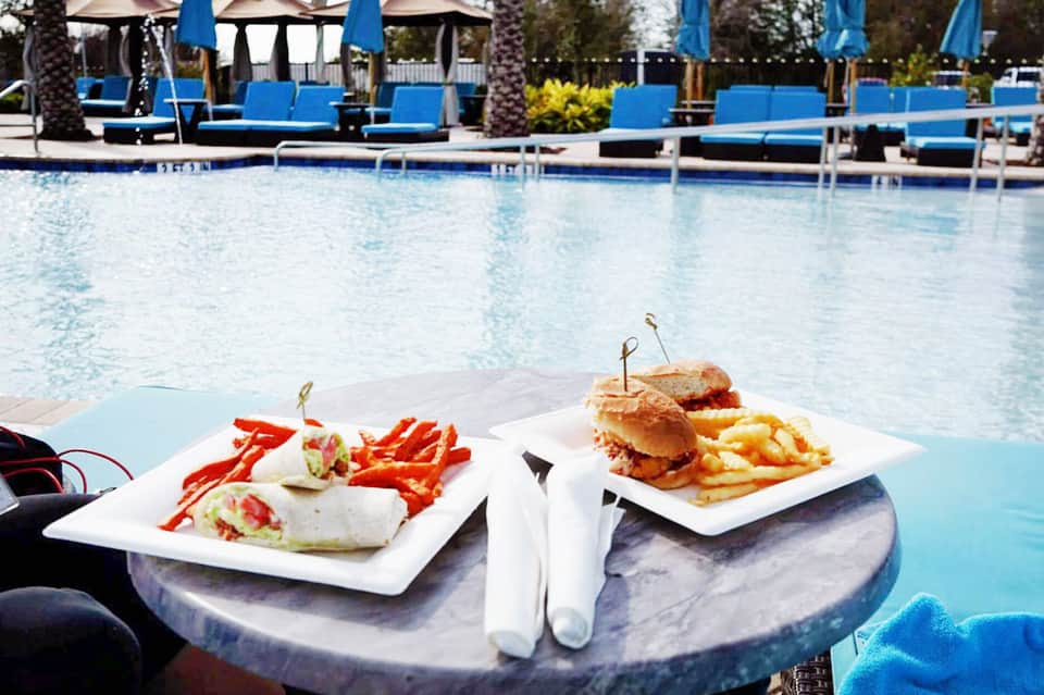 Poolside dining with wraps and burgers on white plates by the pool with blue loungers