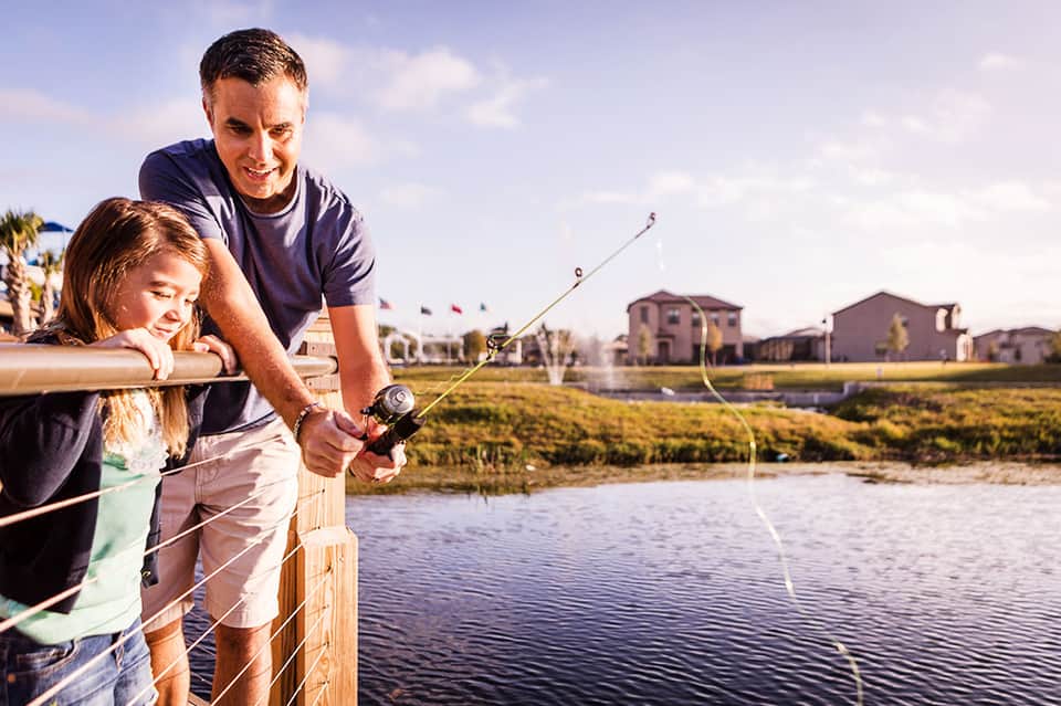 Adult and child fishing together from a wooden dock overlooking a residential community and waterway