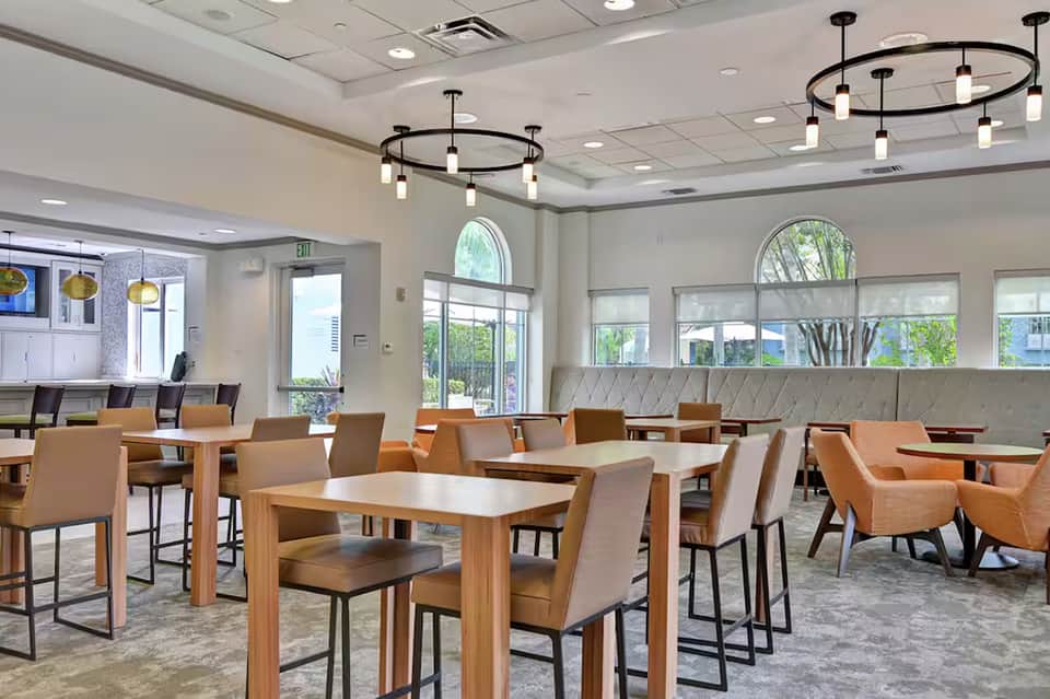 Modern dining area with wooden tables, orange chairs, and large windows overlooking greenery