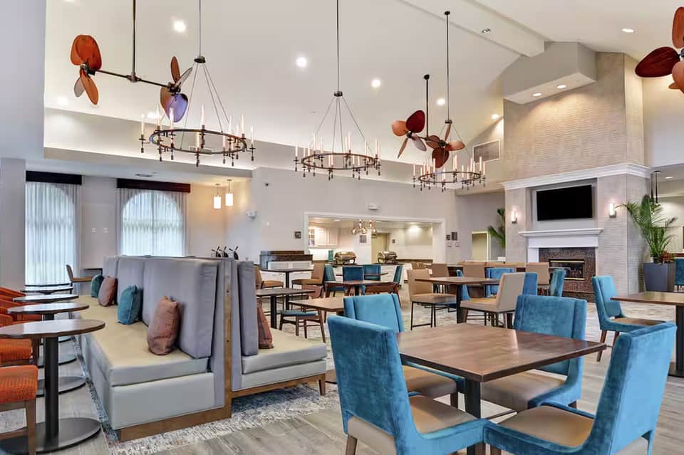 Modern hotel lounge with blue velvet chairs, gray sectional sofas, hanging copper light fixtures, and decorative plant sculptures