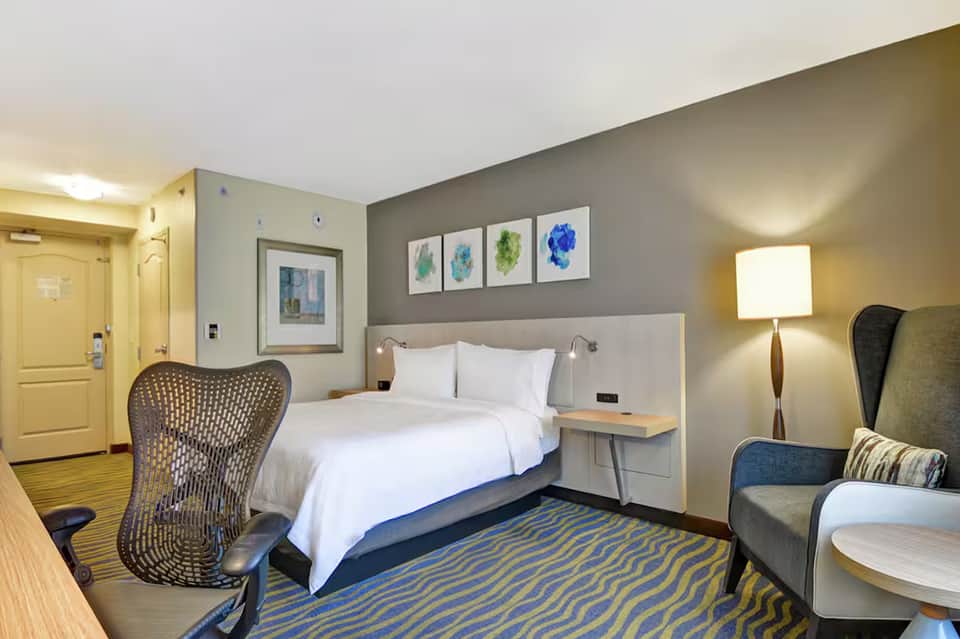 Modern hotel bedroom with queen bed, gray headboard, colorful abstract wall art, and contemporary furnishings