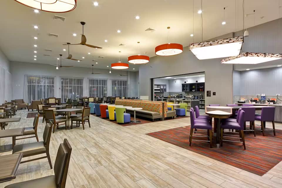 Modern resort dining and lounge area with colorful seating, orange pendant lights, and floor-to-ceiling windows