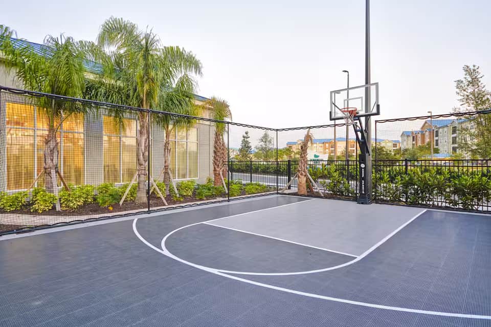 Outdoor basketball court with palm trees, yellow building, and black metal railings overlooking residential area