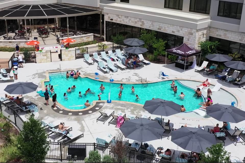 Aerial view of resort swimming pool with lounge chairs, umbrellas, and guests enjoying the water