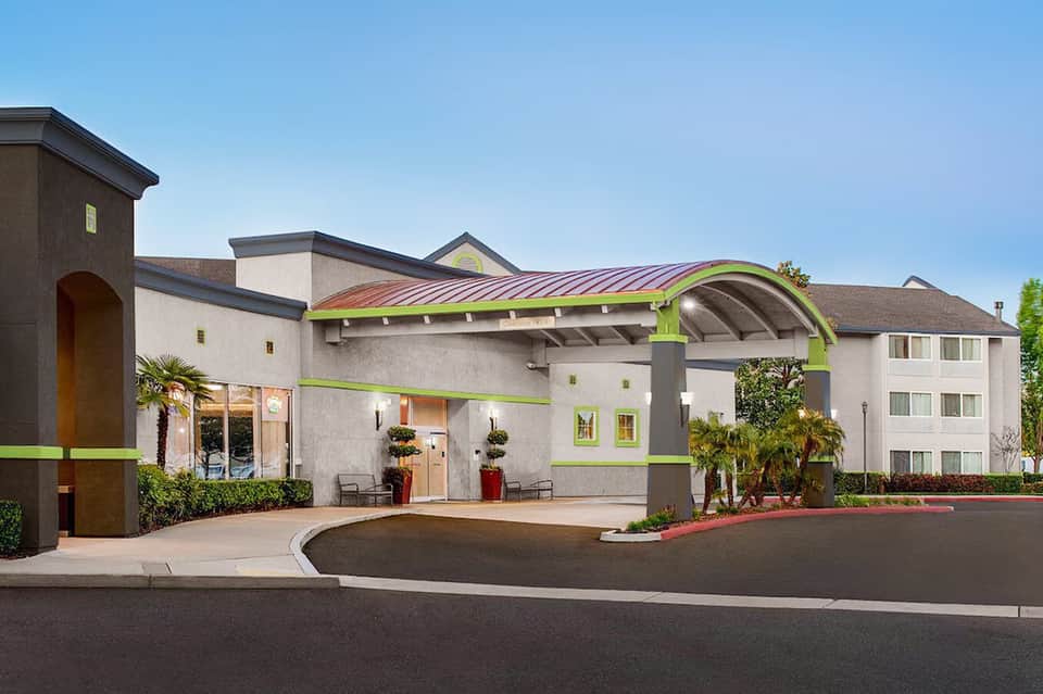 Modern hotel exterior with lime green accents, curved architectural features, and palm trees in landscaping