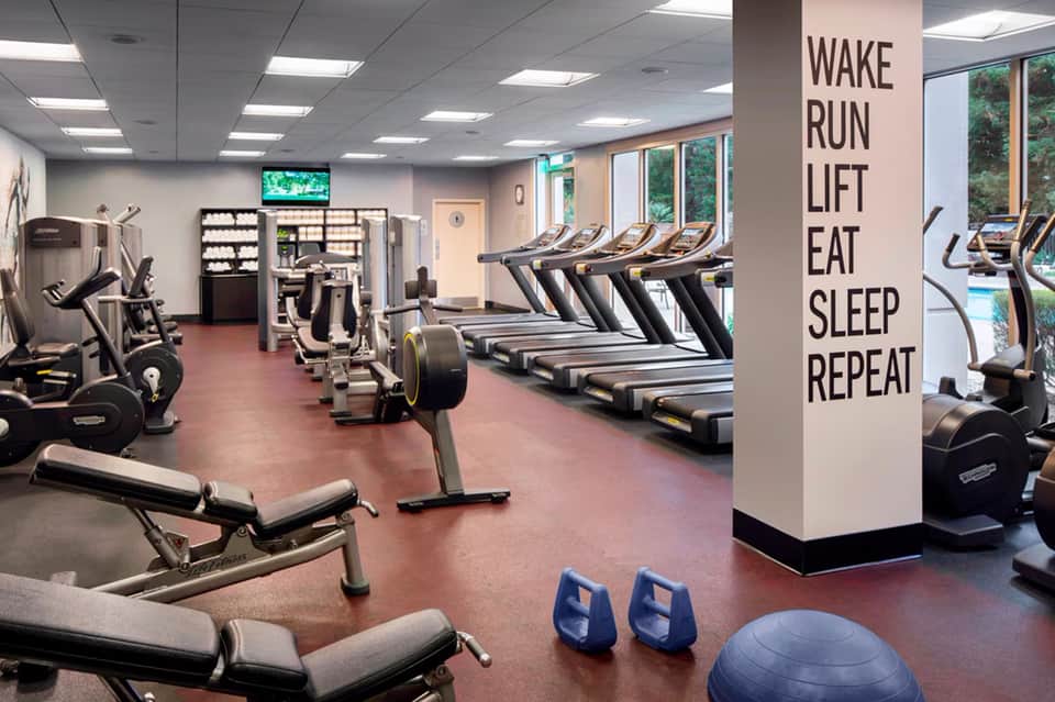 Fitness center with treadmills, exercise equipment, and motivational wall text in neutral tones