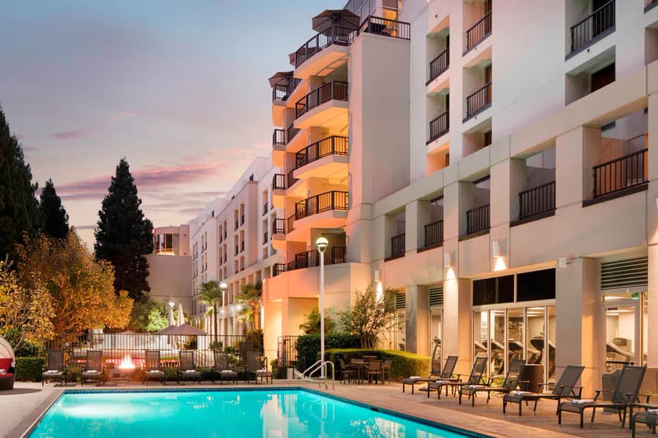 Luxury hotel exterior at dusk with illuminated balconies, pool, and lounge seating area