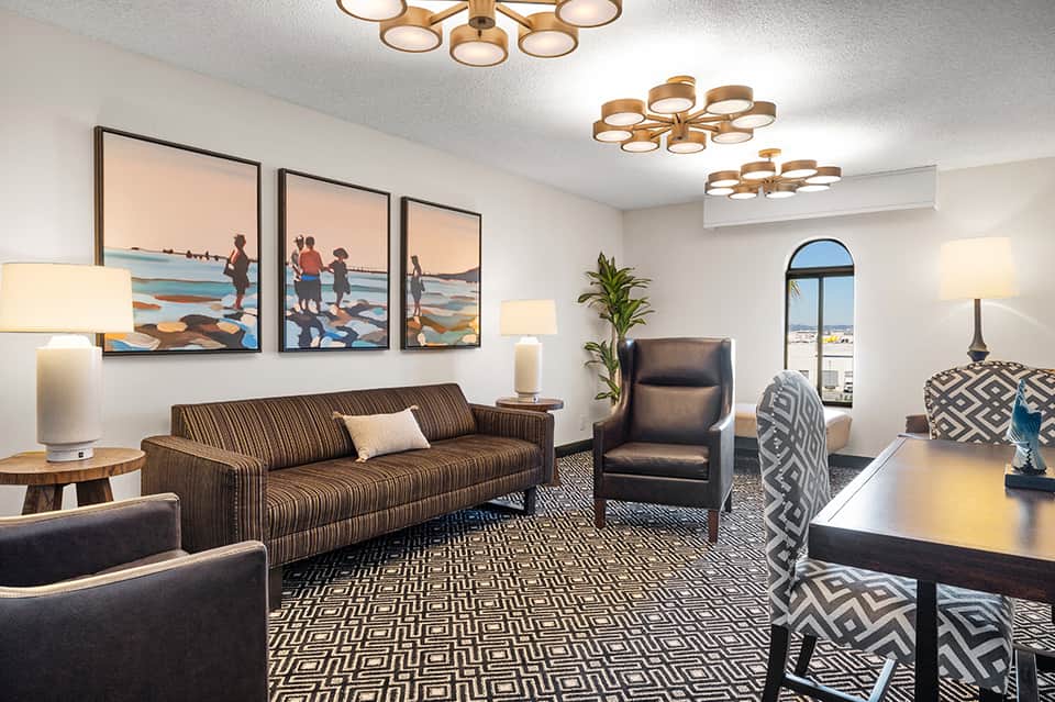 Modern hotel lounge with striped sofa, geometric patterned rug, framed beach artwork, and brass ceiling lights