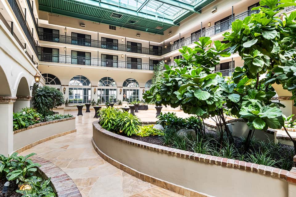 Indoor atrium with curved planters, lush greenery, arched windows, and multi-level balconies