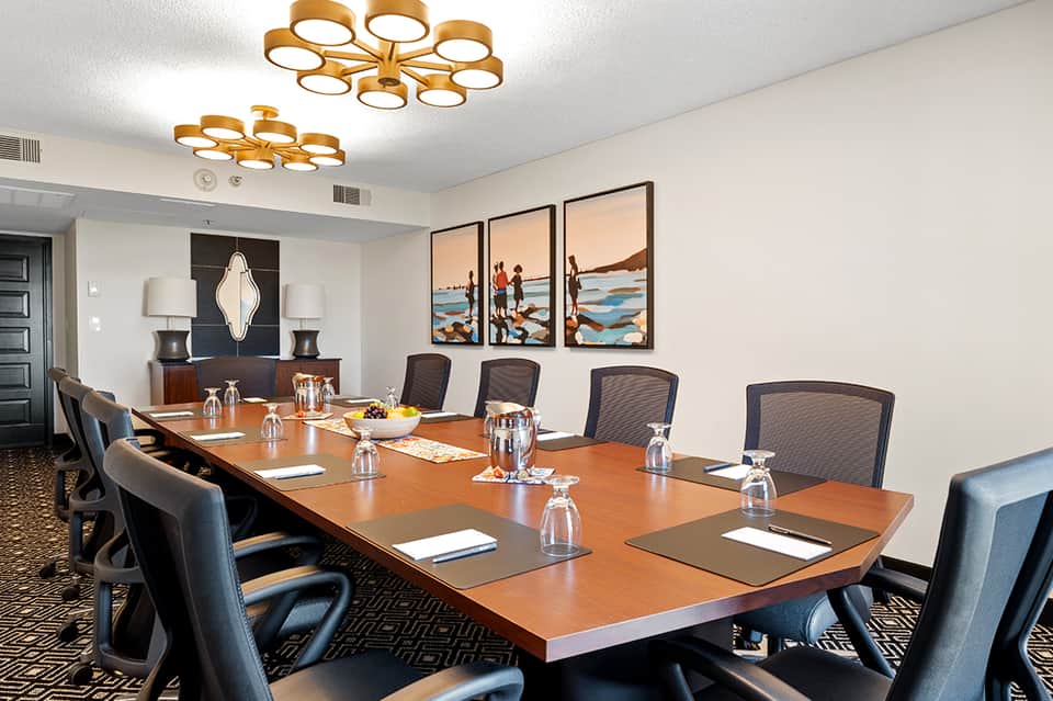Modern conference room with long wooden table, black mesh chairs, and colorful beach artwork