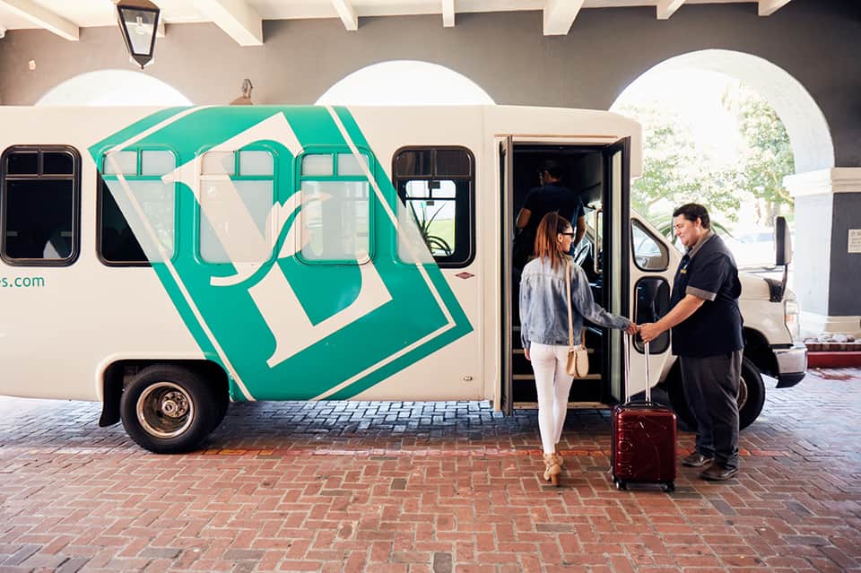 Turquoise and cream branded shuttle bus with staff assisting guest with luggage at hotel entrance