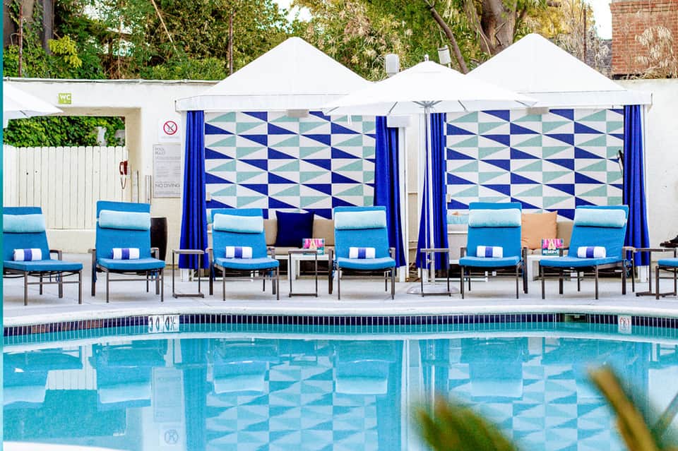 Resort pool with blue loungers under white tent canopies with geometric patterned backdrops and trees