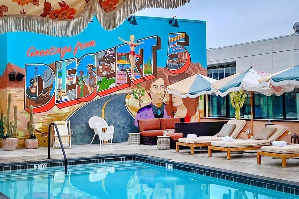 Retro-style pool deck with vintage mural reading 'Greetings from Desk 5' and lounge seating