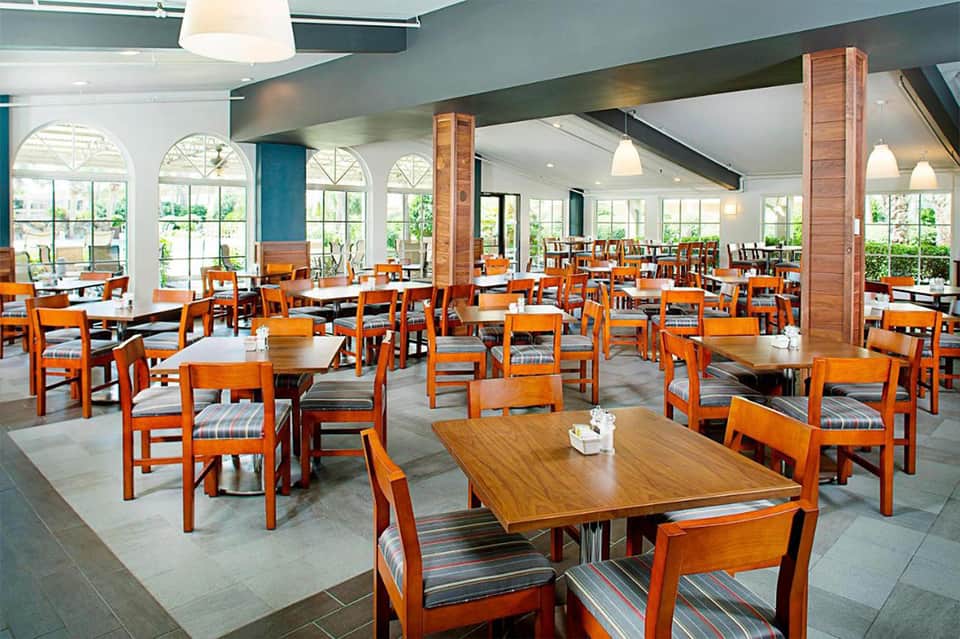 Spacious dining room with orange wooden chairs, striped seat cushions, arched windows, and brick columns
