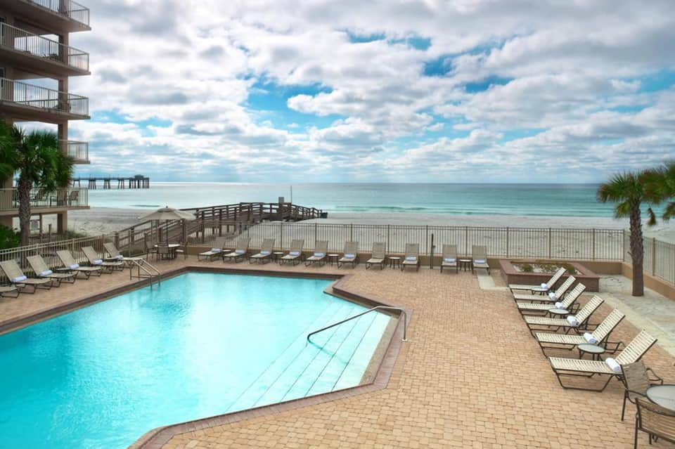 Beachfront resort pool with lounge chairs overlooking ocean and wooden pier