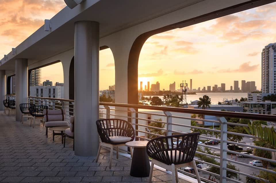 Waterfront terrace at sunset with modern seating, city skyline and bay views across the railing