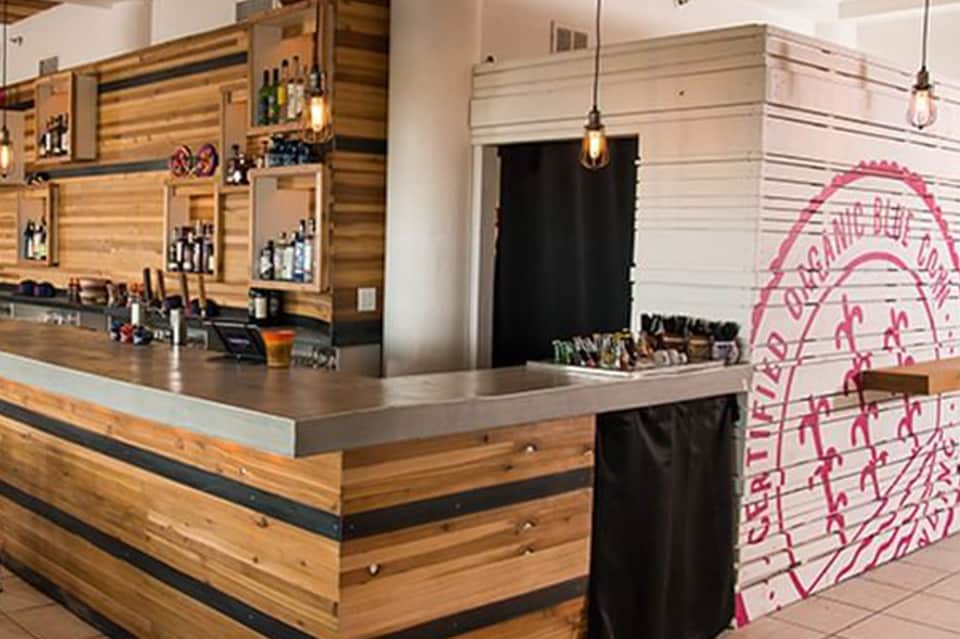 Contemporary bar interior with wooden slat walls, pendant lighting, counter seating, and pink neon wall art.