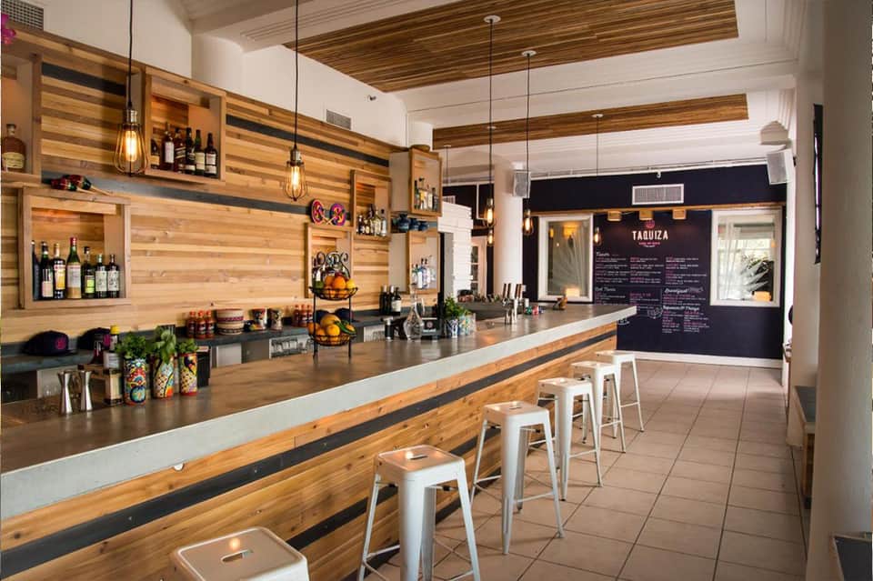 Modern bar interior with wooden striped walls, pendant lighting, and white metal bar stools along counter