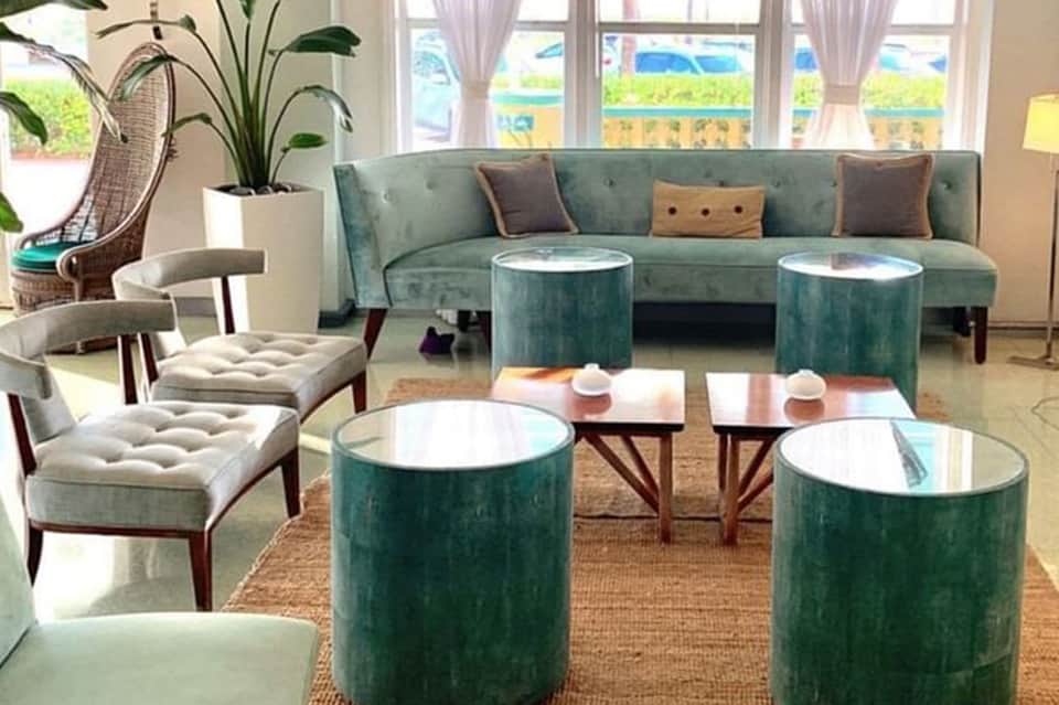 Modern hotel lounge with teal velvet sofa, cylindrical ottoman tables, and natural light from large windows