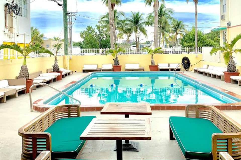Bright yellow-walled courtyard with rectangular turquoise swimming pool, lounge chairs, and palm trees