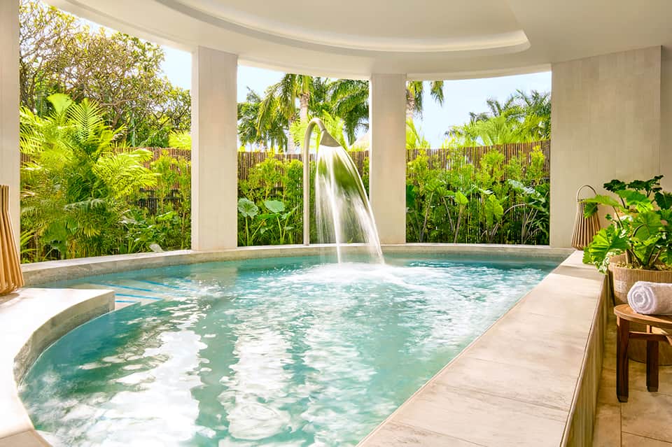 Indoor spa pool with waterfall, large windows overlooking tropical vegetation