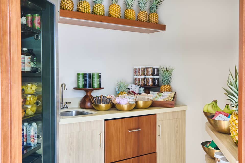 Modern kitchenette with pineapples on shelf, gold bowls, and green refrigerator stocked with beverages