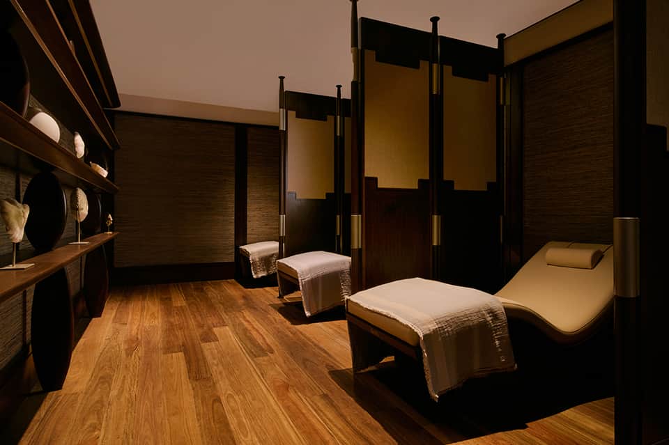 Luxury spa treatment room with wooden furnishings, massage beds, and warm amber and black interior design.
