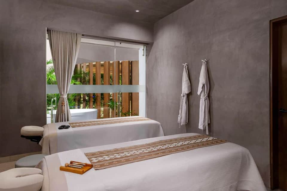 Spa treatment room with massage bed, wooden accents, natural light, and towel racks