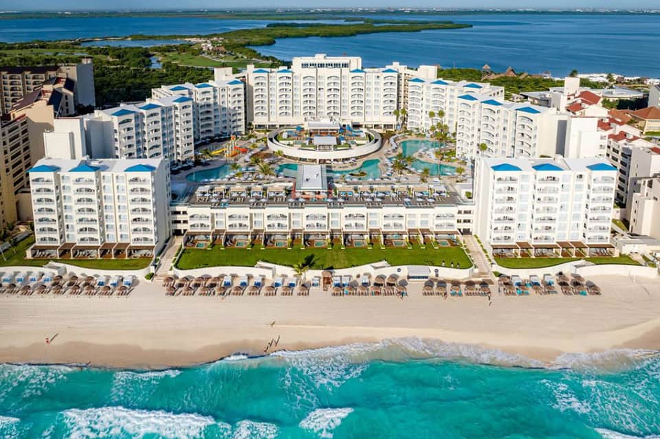 Beachfront resort with white multi-story buildings, curved pool area, and turquoise ocean waves