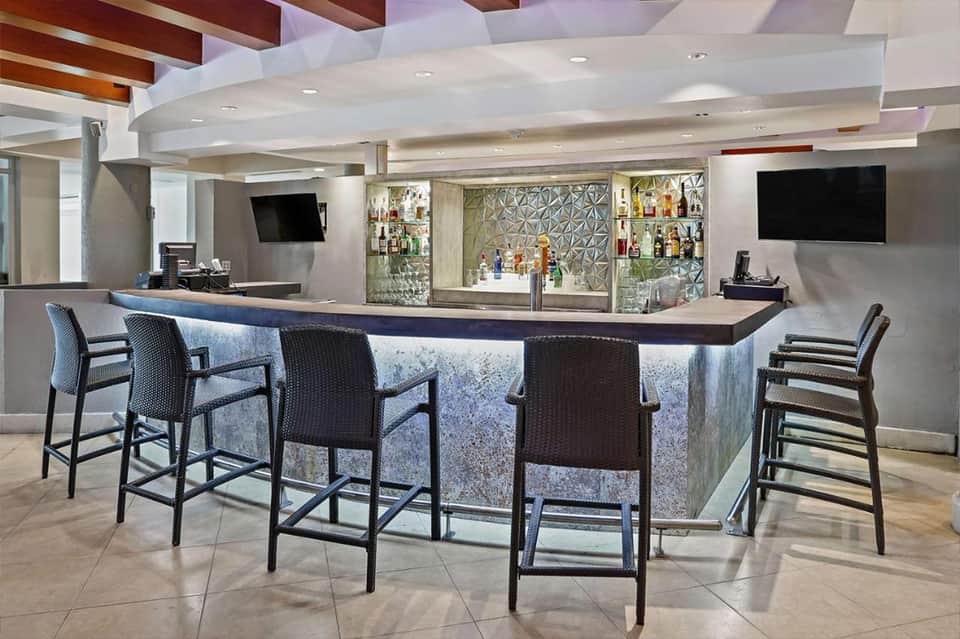 Contemporary bar counter with black seating, geometric patterned backing, and illuminated shelving