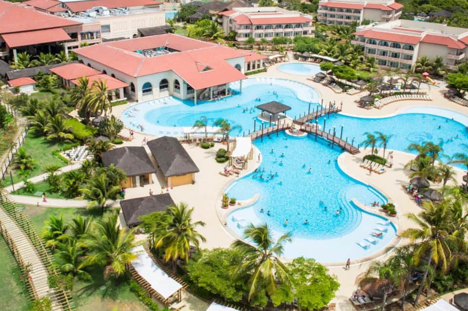 Aerial view of large resort with multiple swimming pools, red-roofed buildings, and tropical landscaping