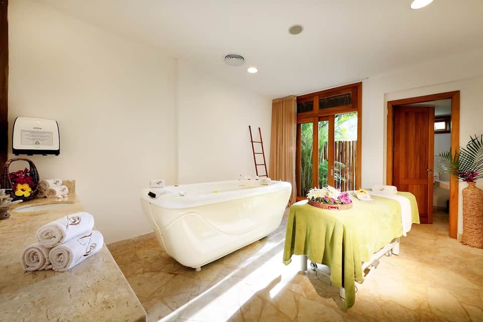 Spa treatment room with soaking tub, massage table, and tropical flowers