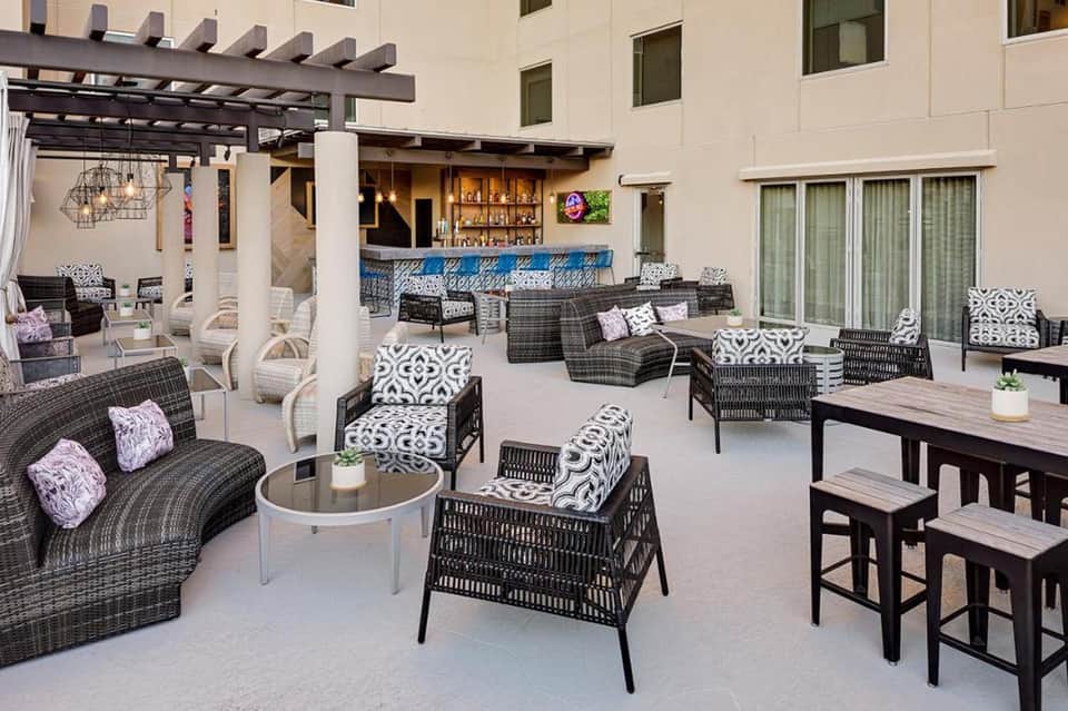 Upscale outdoor patio with wicker lounge chairs, patterned cushions, bar, and dining tables