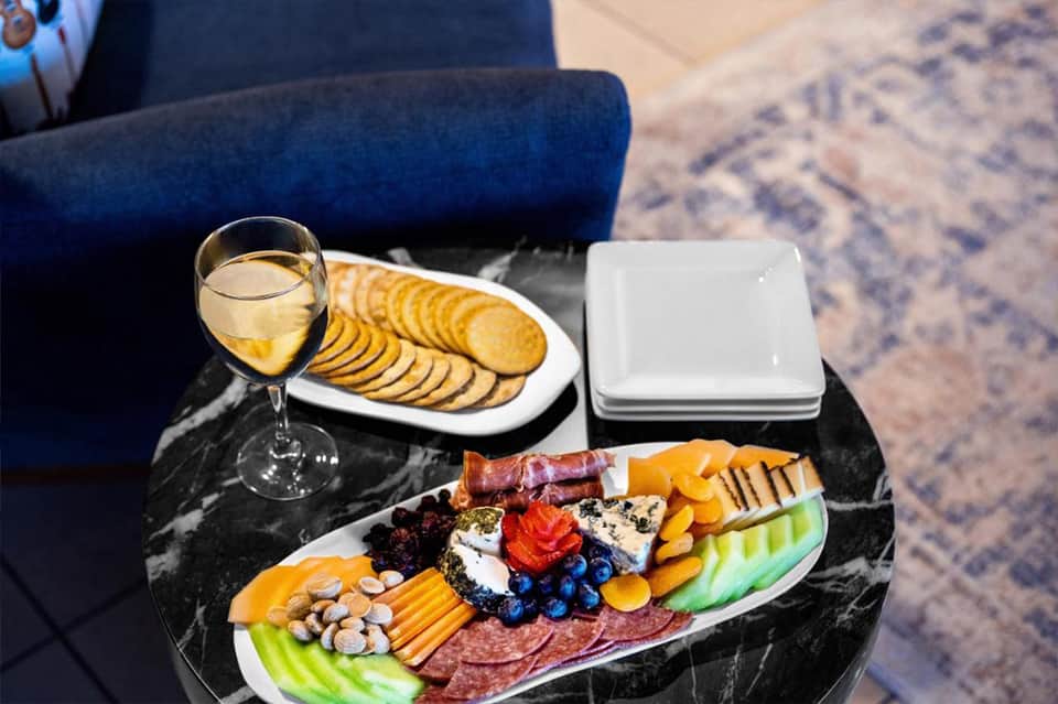 Charcuterie board with cured meats, cheeses, crackers, nuts, and berries beside a glass of white wine on a marble table