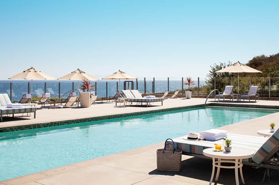 Oceanfront resort pool with turquoise water, white umbrellas, lounge chairs, and sea views